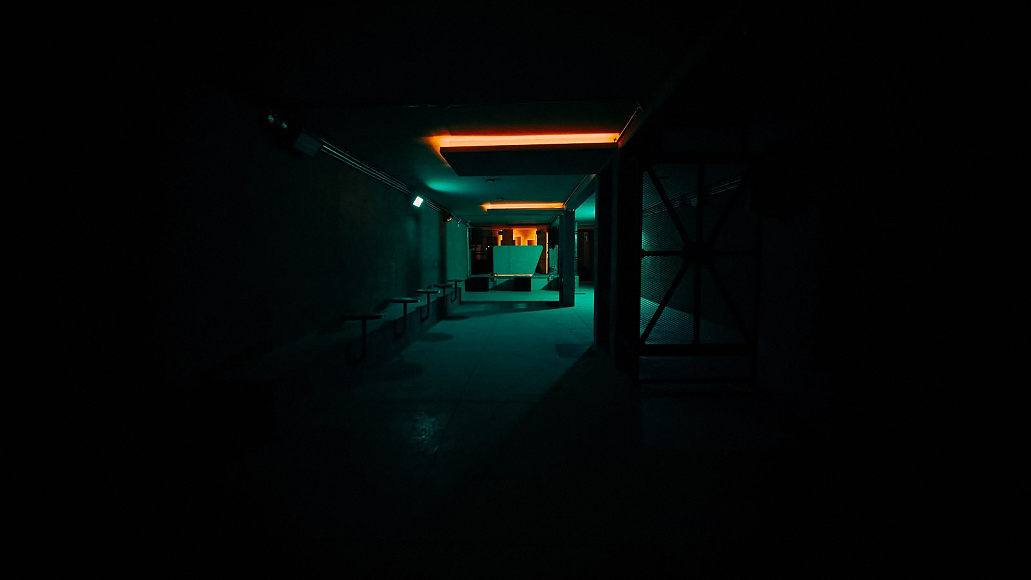 Pasillo de DUNA CLUB en penumbra, con un tubo fluorescente naranja en el techo y luz cyan al fondo.
