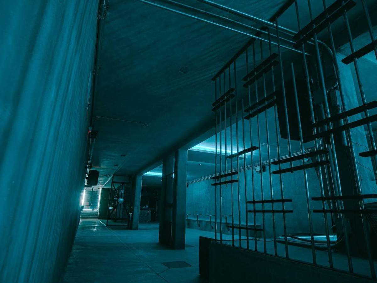 Pasillo de DUNA CLUB con columnas de concreto, barandal de acero y luz fluorescente cyan.